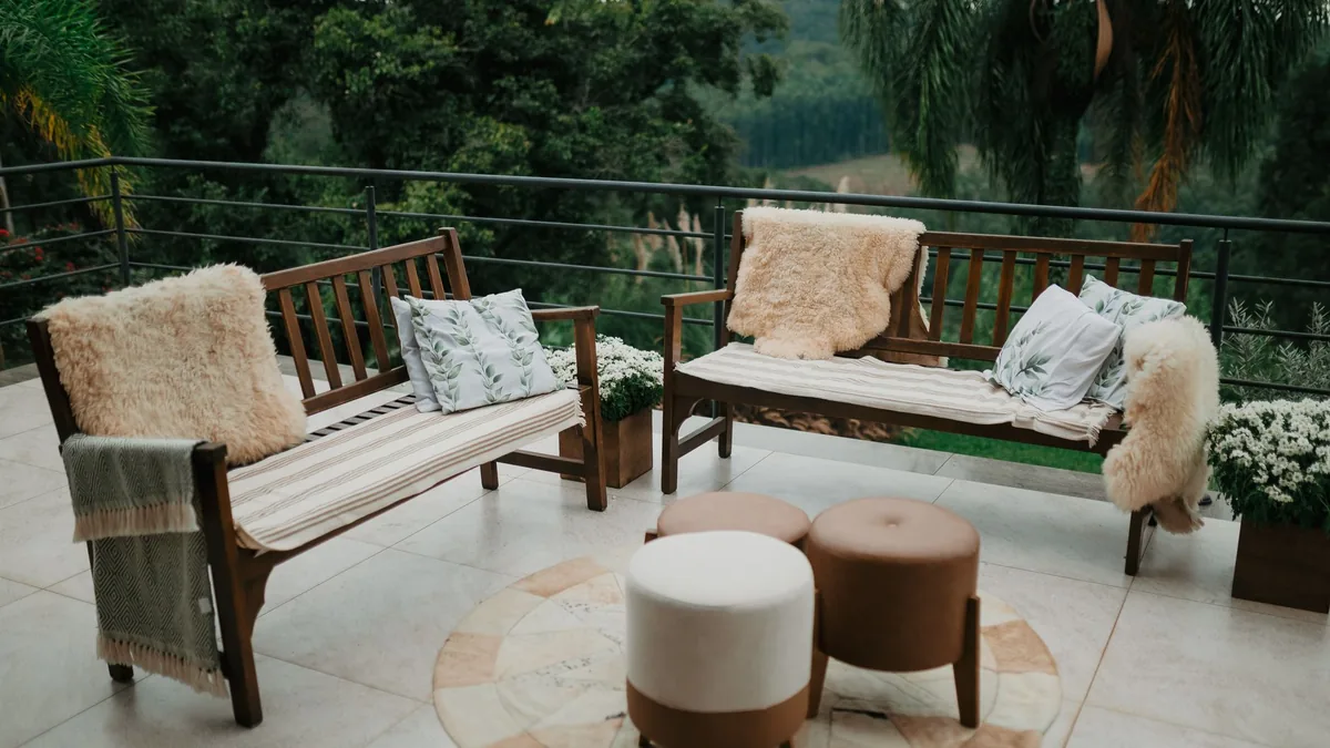 Dos bancos de madera con cojines y una manta de borreguito en una terraza, con vistas a un paisaje verde de fondo.